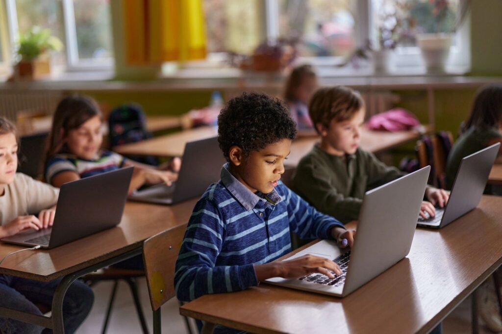 Black schoolboy e-learning over laptop with his friends in the classroom.